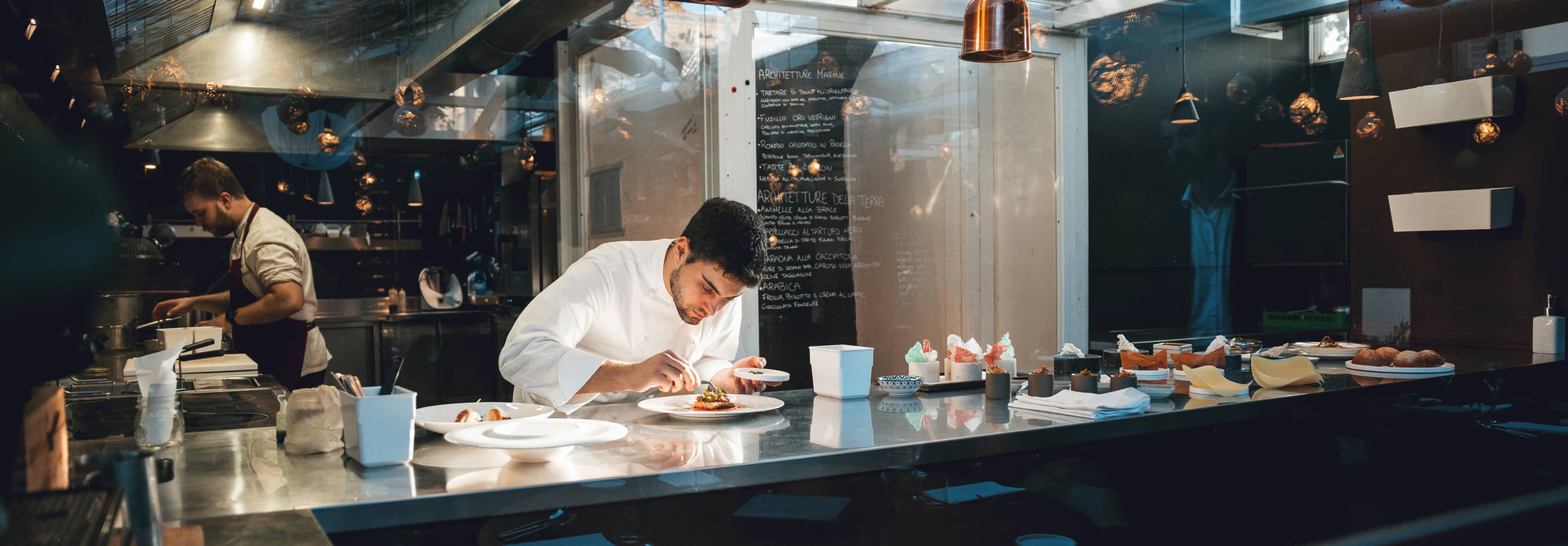 Chef in a high-end restaurant kitchen attentitively plating a meal