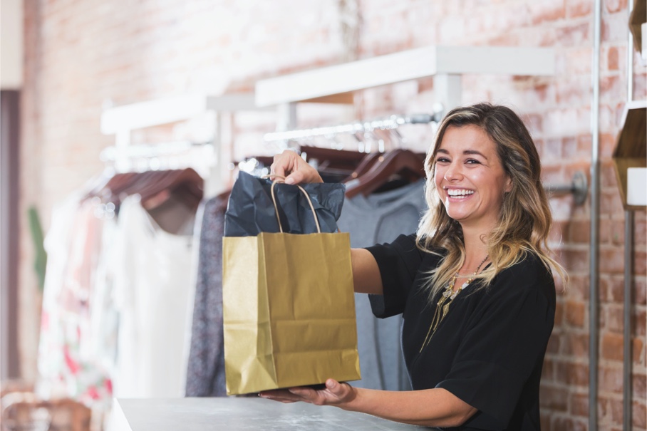 grinning woman holding a brown paper shopping bag
